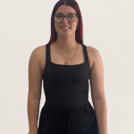 Portrait of a woman with dark hair dyed red at the ends, wearing glasses and a black sleeveless top, smiling at the camera against a light background.